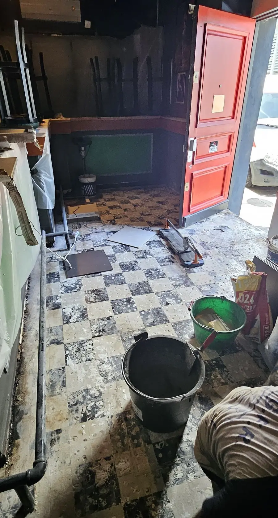 Entrée du club avant travaux : ancien damier noir et blanc usé en cours de dépose, support mis à nu, seaux de chantier.