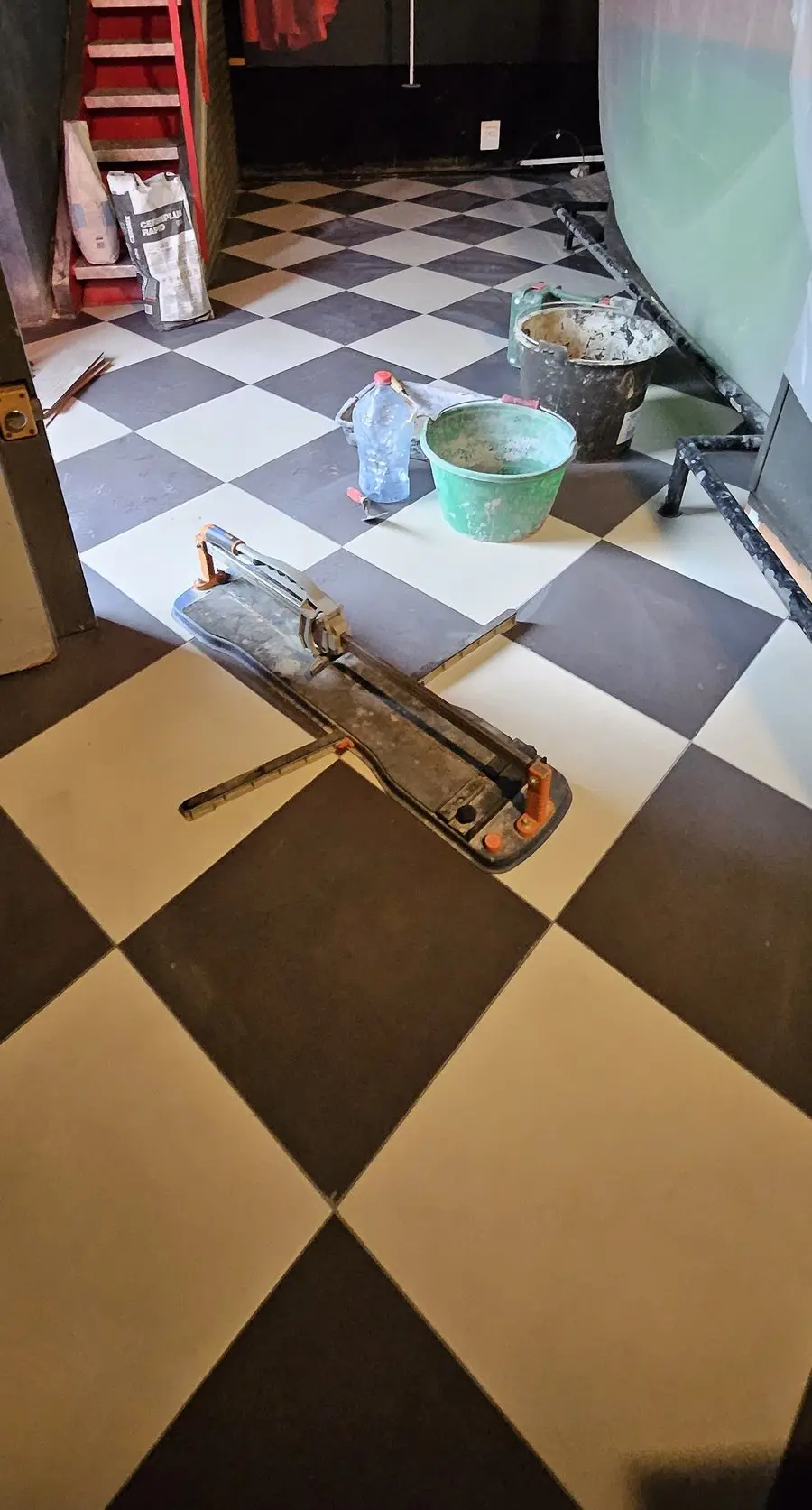 Pose du nouveau damier en diagonale, coupe-carreaux et seaux de colle sur le chantier.