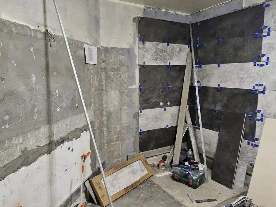 Pose du carrelage mural grand format, croisillons de calage en place et niveau posé contre le mur.