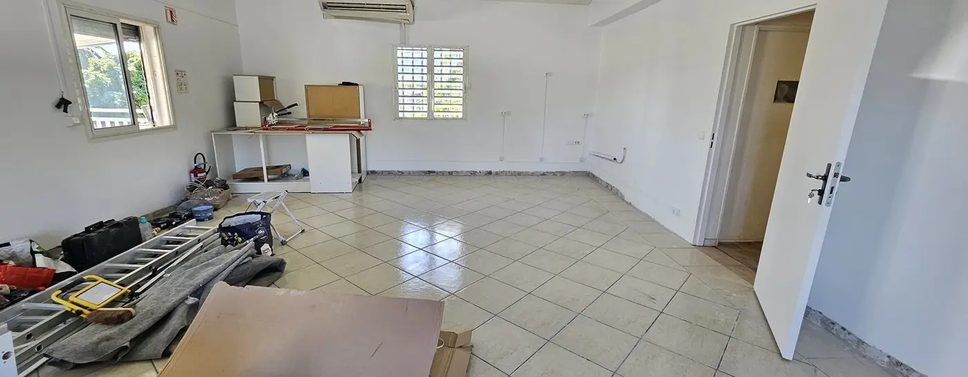 Vue en enfilade de la salle avant travaux : carrelage beige, plinthes déposées, poste de découpe installé au fond.