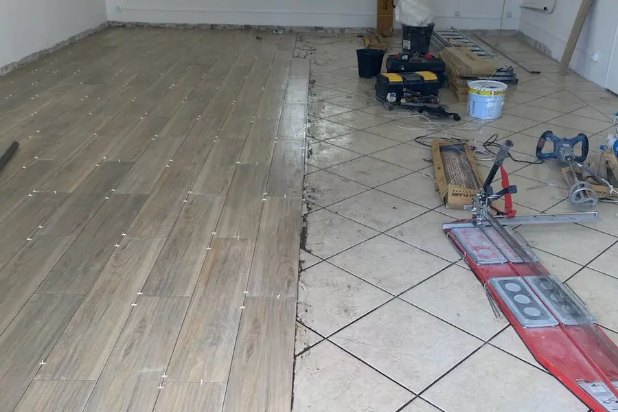 Pose en cours : les lames effet bois rejoignent l’ancien carrelage beige sur une ligne franche, croisillons et coupe-carreaux en place.