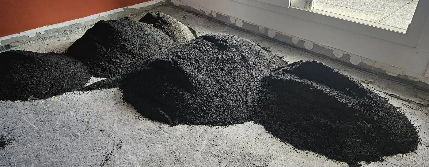 Tas de sable volcanique noir répartis sur le support avant montage de la chape, sacs de ciment à côté.